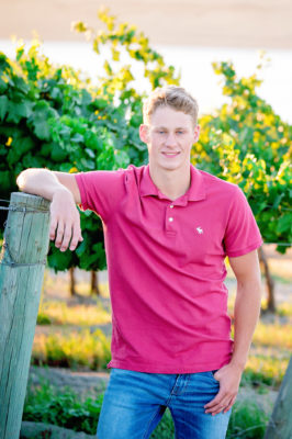 Senior guy posing in his family vineyard in a red shirt.