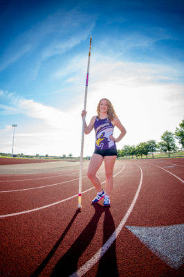 Girl standing with a pole vault on a track.