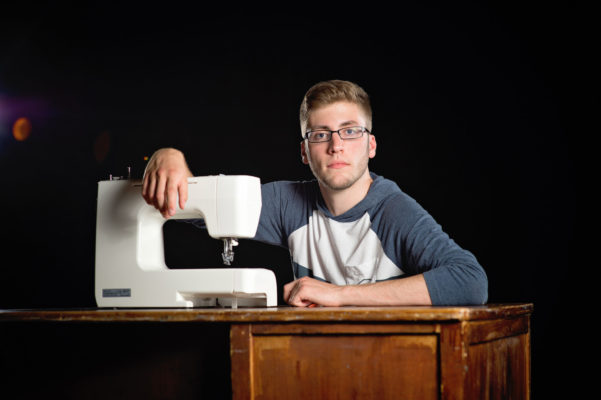 Senior guy portrait on stage with a sewing machine.