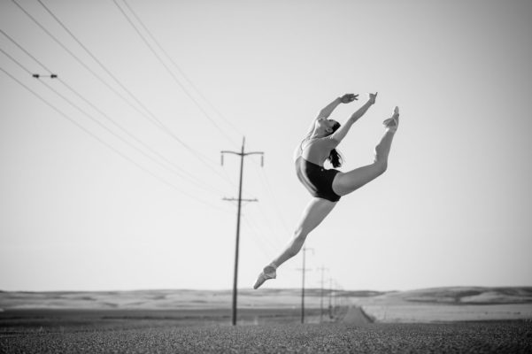 Black and White portrait of ballet dancer jumping on country road.
